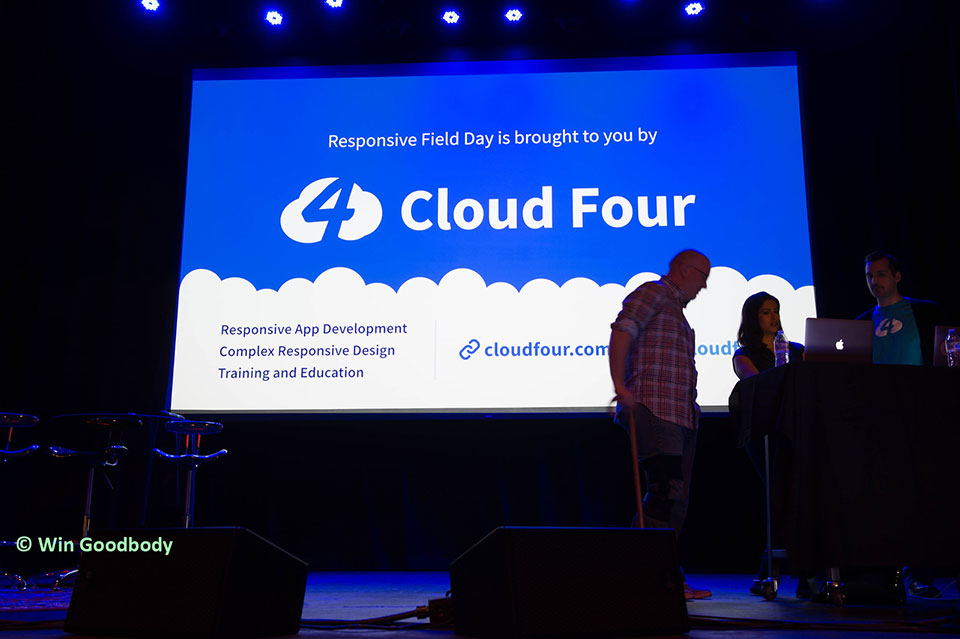 Jason Grigsby, Yesenia Perez-Cruz and Tyler Sticka stand on stage against a photo crediting Cloud Four with the event. (Photo ©️ Win Goodbody)