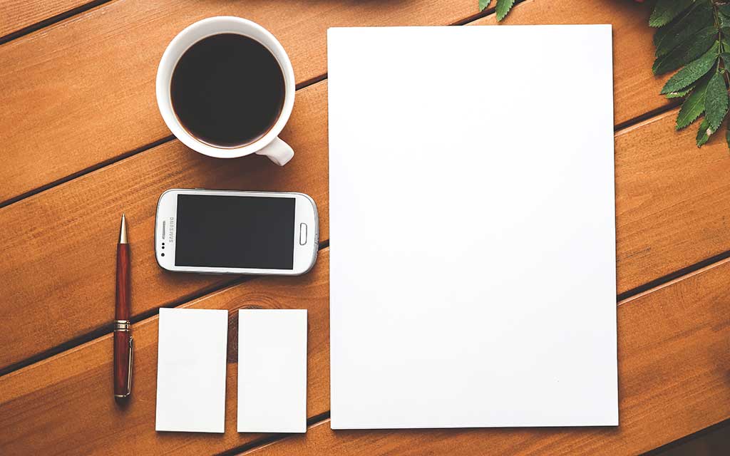 A coffee cup, smartphone and pads of paper on a desk