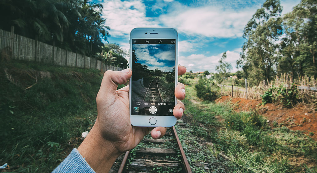 Person holding an iPhone with the camera looking at train tracks heading into the distance