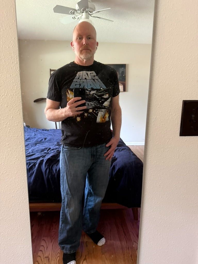 I photo of me taken in a mirror. I'm wearing jeans and a black Star Wars shirt. I'm not thin, but I'm much healthier than I was at performance.now() in 2024.